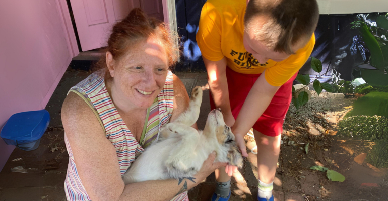 A mother, Rebecca, and son, John, smiling and playing with a small dog