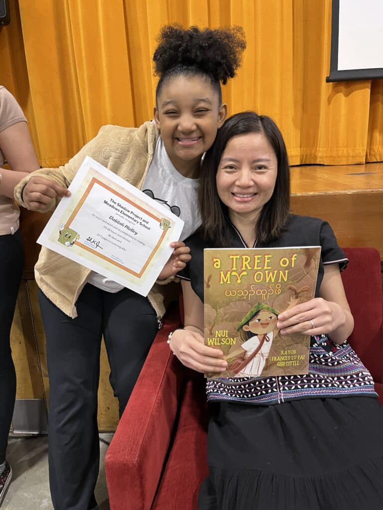 Nui Wilson posing with her book and a student in the Reading Mentor Program.